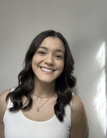 A light-skinned woman with brown eyes and brown medium-length hair. She is wearing a white top with a gold necklace.